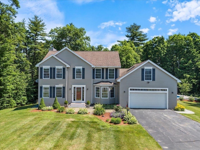 colonial inspired home featuring a front lawn, roof with shingles, driveway, and a chimney