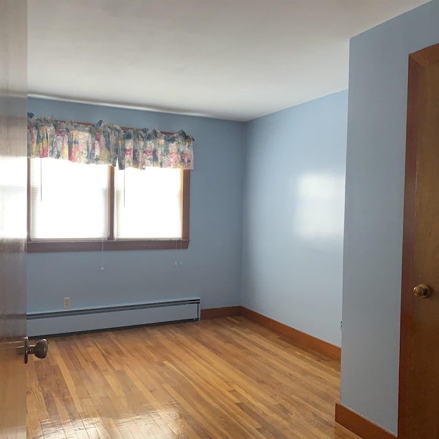 spare room with a baseboard heating unit, hardwood / wood-style flooring, and baseboards