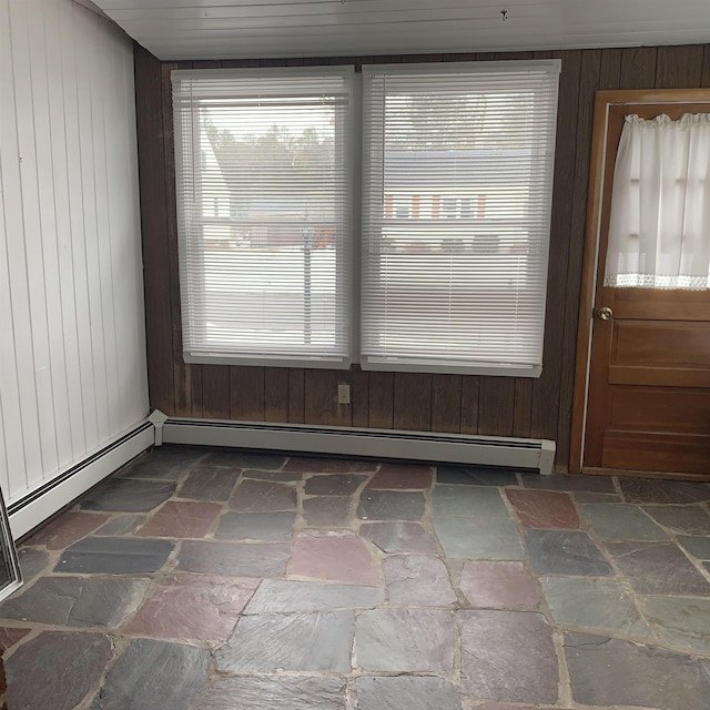 unfurnished dining area with a baseboard radiator, wooden walls, and stone finish floor