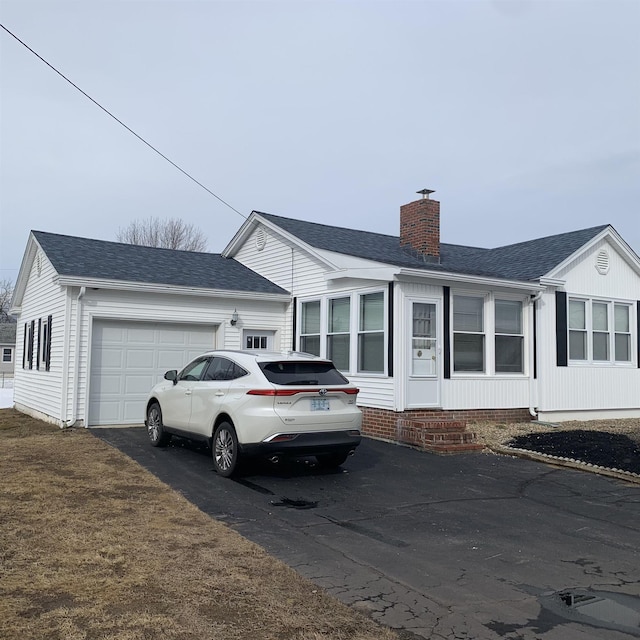 view of front of house featuring aphalt driveway, a garage, a chimney, and a shingled roof