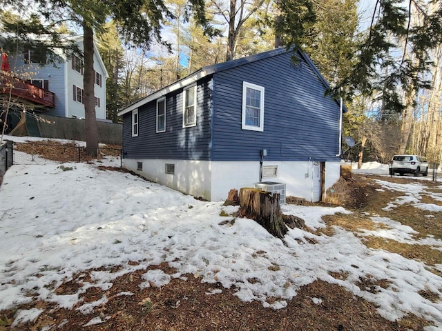 view of snowy exterior with central AC unit and fence