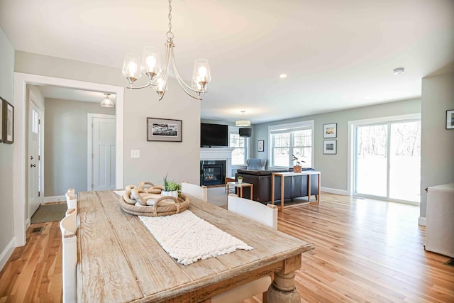 dining space featuring a glass covered fireplace, light wood-style flooring, visible vents, and baseboards