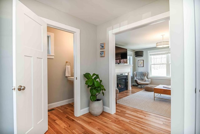 hall featuring a wall unit AC, wood finished floors, baseboards, and visible vents