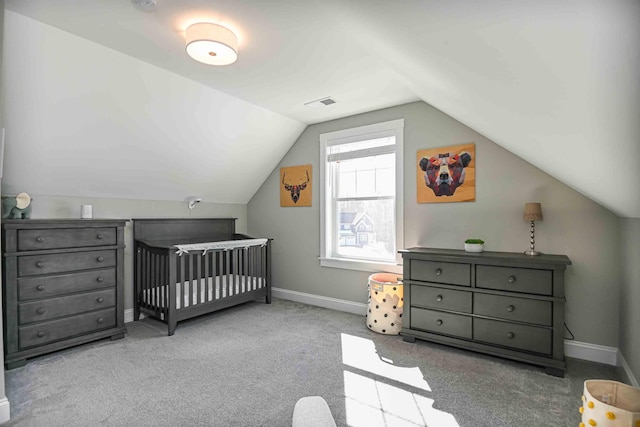 carpeted bedroom featuring a crib, lofted ceiling, visible vents, and baseboards