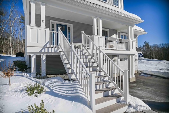 snow covered property entrance featuring a porch and a garage