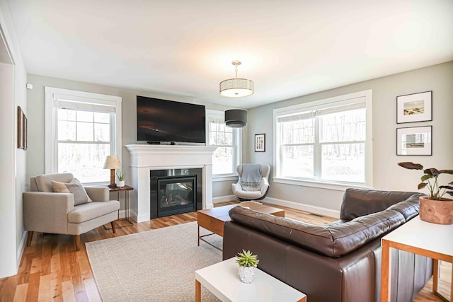 living area featuring a glass covered fireplace, light wood-style flooring, and baseboards