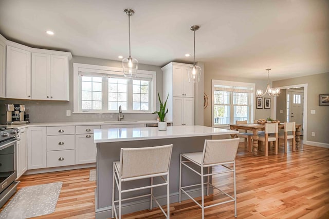 kitchen with stainless steel range with electric stovetop, white cabinetry, light countertops, and a sink