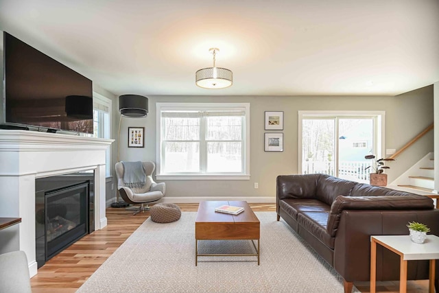 living area featuring light wood finished floors, a glass covered fireplace, plenty of natural light, and stairs