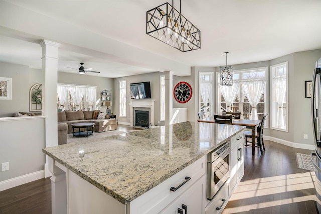 kitchen featuring a fireplace, stainless steel microwave, decorative columns, and dark wood-style floors