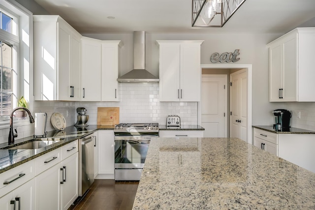 kitchen featuring a sink, white cabinetry, dark stone counters, appliances with stainless steel finishes, and wall chimney exhaust hood