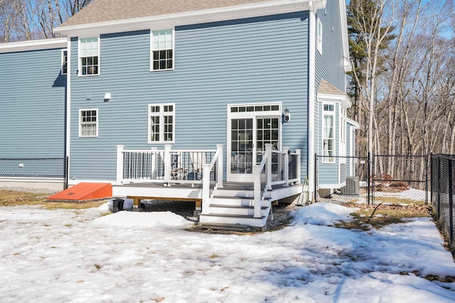 snow covered house with a wooden deck, roof with shingles, and fence