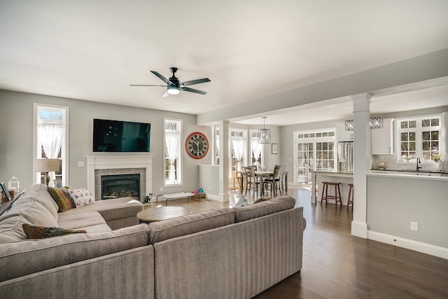 living area with dark wood-type flooring, decorative columns, a fireplace, and a wealth of natural light