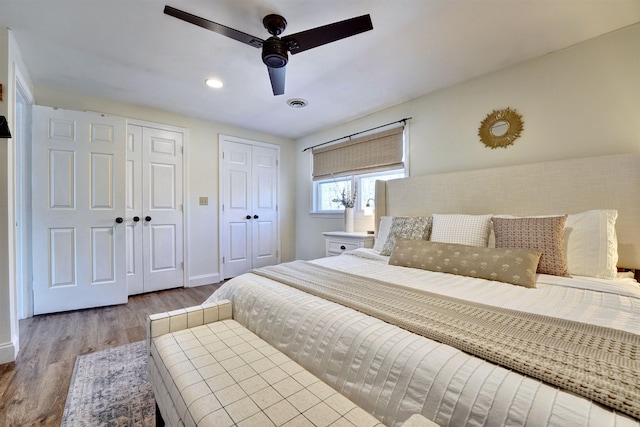 bedroom featuring wood finished floors, visible vents, baseboards, ceiling fan, and multiple closets