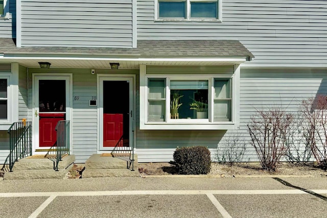 doorway to property featuring uncovered parking and a shingled roof