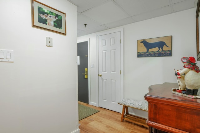 hall with a drop ceiling, baseboards, and light wood-style floors