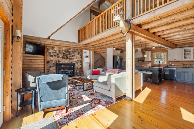 living area with log walls, a high ceiling, a stone fireplace, hardwood / wood-style flooring, and stairs