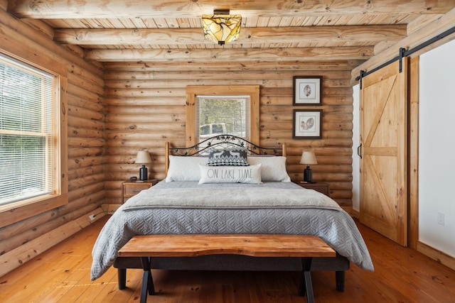 bedroom with a barn door, beam ceiling, multiple windows, and light wood-style flooring