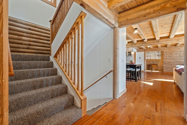 stairway with rustic walls, beam ceiling, wood ceiling, and wood-type flooring