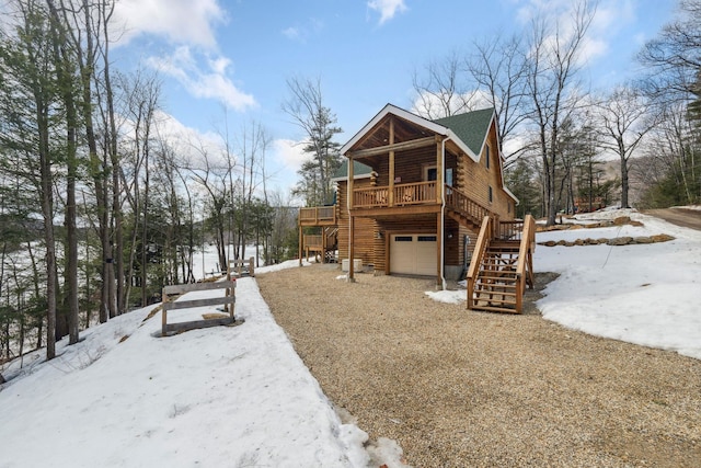 snow covered property with stairway, a garage, and log exterior