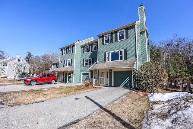 view of property featuring an attached garage, a chimney, and driveway