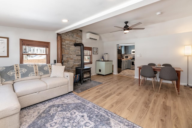 living room featuring light wood finished floors, ceiling fan, vaulted ceiling, a wood stove, and a wall mounted AC