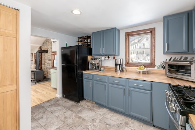 kitchen with blue cabinets, stainless steel range with gas cooktop, a wood stove, and freestanding refrigerator