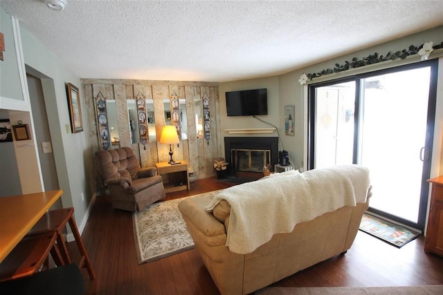 living area with a glass covered fireplace, a textured ceiling, a healthy amount of sunlight, and wood finished floors