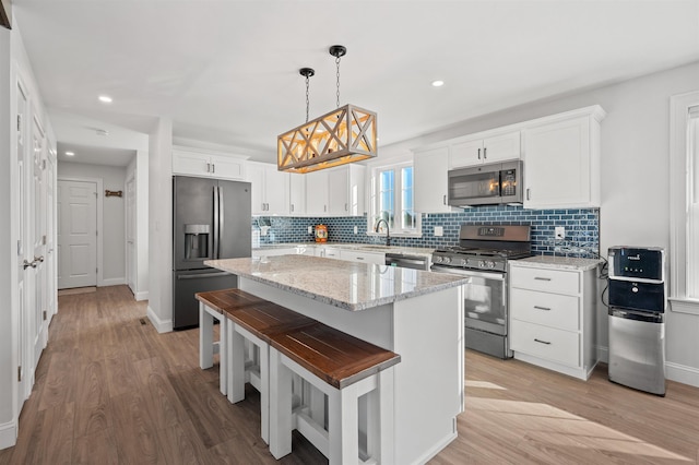 kitchen with a center island, white cabinetry, stainless steel appliances, light wood-style floors, and decorative backsplash