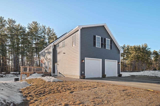 view of property exterior featuring a deck, an attached garage, and driveway