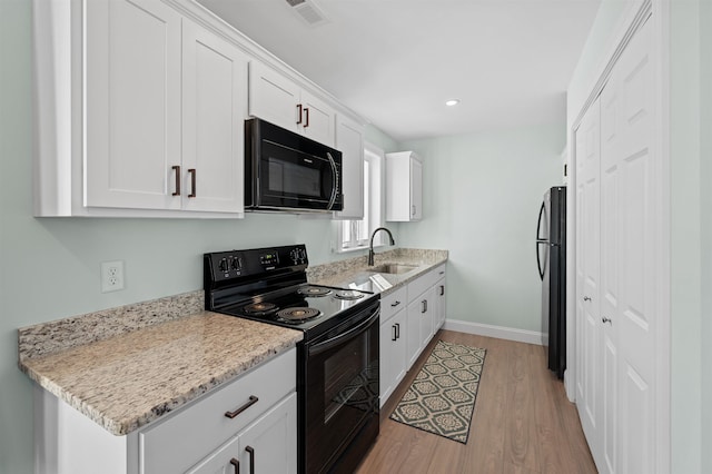 kitchen with visible vents, black appliances, light wood-style flooring, a sink, and white cabinets