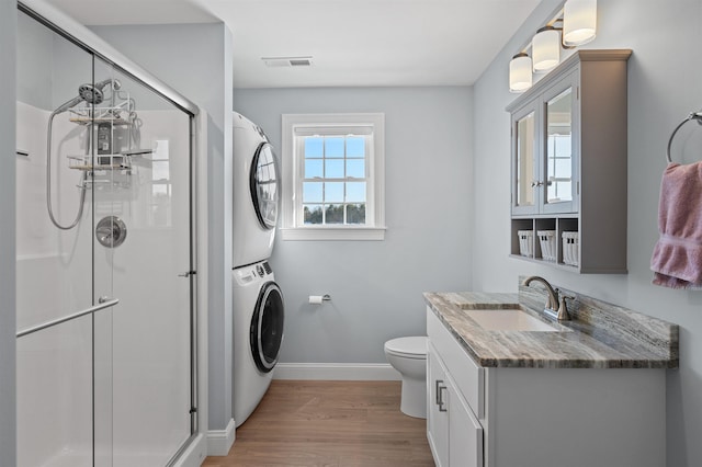 full bathroom with a stall shower, wood finished floors, stacked washer / drying machine, baseboards, and vanity