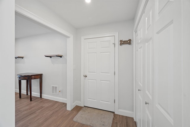 hall featuring visible vents, baseboards, and wood finished floors