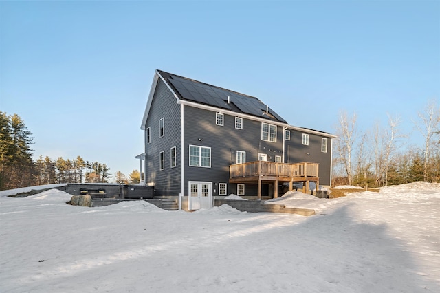 snow covered back of property with solar panels and a deck