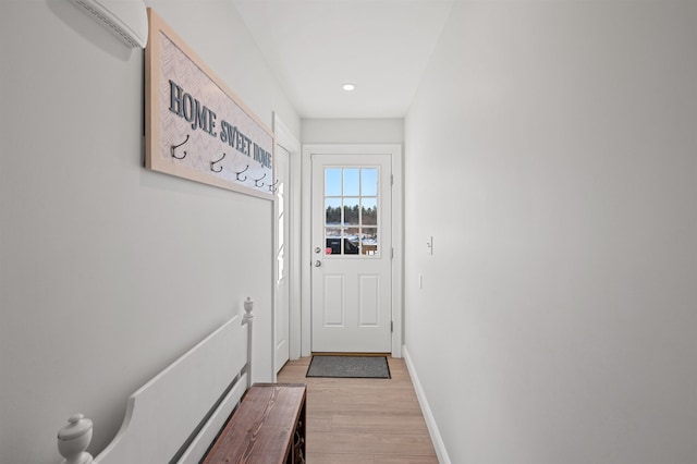 doorway to outside with light wood-style flooring, a wall mounted air conditioner, and baseboards