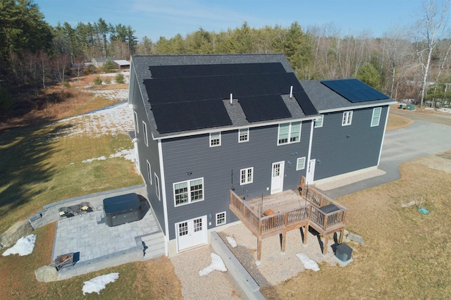 back of house with a patio area, solar panels, a deck, and roof with shingles