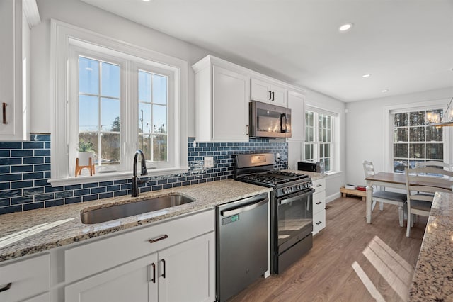 kitchen with light stone countertops, a sink, stainless steel appliances, white cabinets, and light wood-style floors