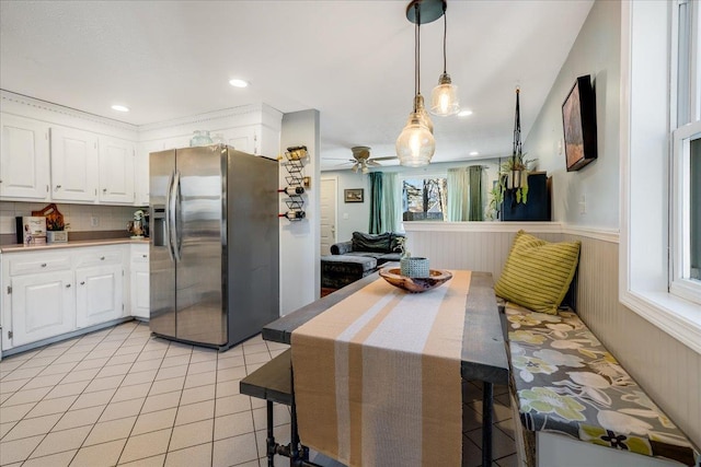 kitchen featuring stainless steel fridge with ice dispenser, a wainscoted wall, pendant lighting, light tile patterned flooring, and white cabinets