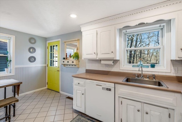 kitchen featuring light tile patterned floors, a wainscoted wall, a sink, white cabinets, and dishwasher