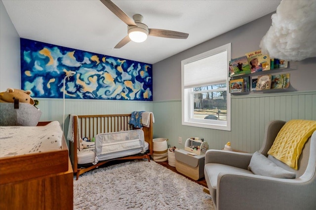 bedroom featuring wood finished floors, a ceiling fan, and wainscoting