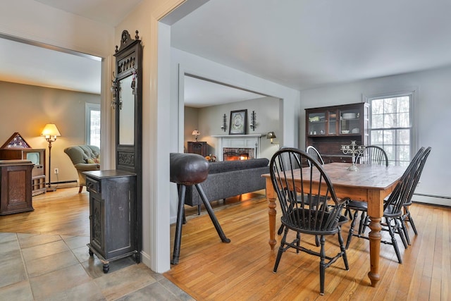 dining space with light wood finished floors, baseboard heating, a baseboard heating unit, and a lit fireplace