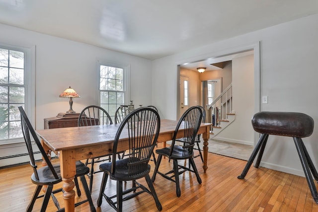 dining area featuring baseboard heating, stairs, light wood-type flooring, and baseboards