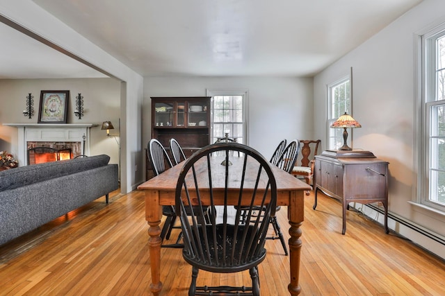 dining area with a healthy amount of sunlight, a warm lit fireplace, and light wood-style floors