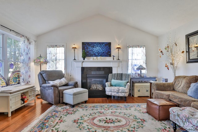 living room featuring a glass covered fireplace, lofted ceiling, and wood finished floors