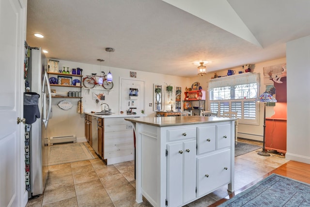 kitchen featuring white cabinetry, baseboard heating, a center island, and freestanding refrigerator