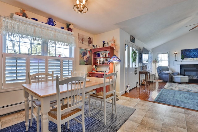 tiled dining room featuring a glass covered fireplace, ceiling fan with notable chandelier, and lofted ceiling