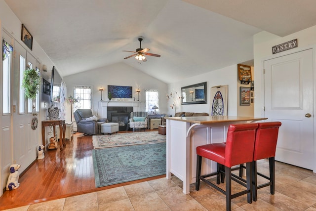 living area featuring a glass covered fireplace, lofted ceiling, a ceiling fan, and light wood finished floors