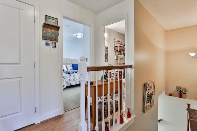 corridor with an upstairs landing, light wood-type flooring, and baseboards