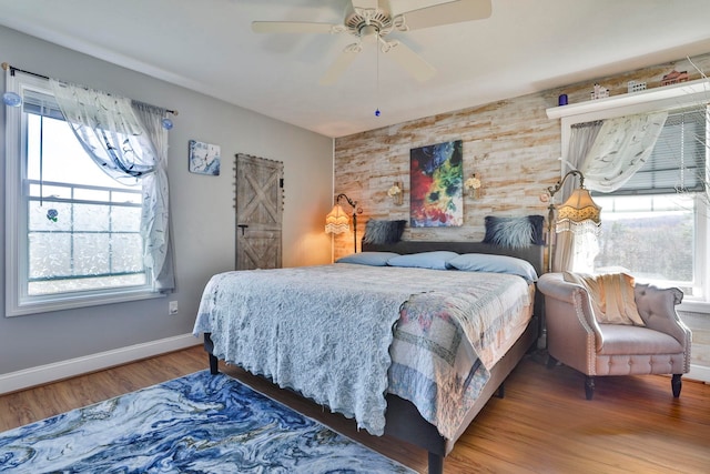 bedroom with multiple windows, an accent wall, baseboards, and wood finished floors