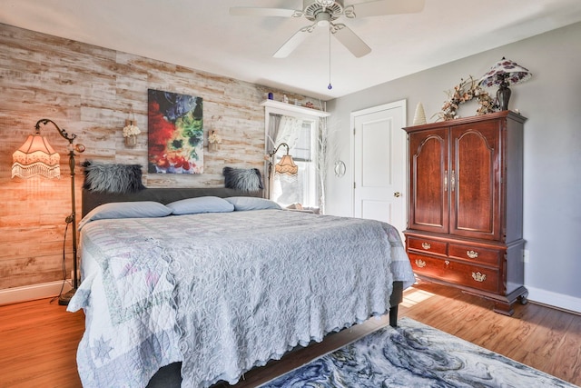 bedroom with light wood finished floors, ceiling fan, wood walls, and baseboards