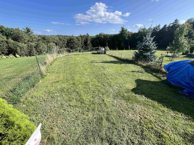 view of yard featuring a rural view, fence, and a view of trees